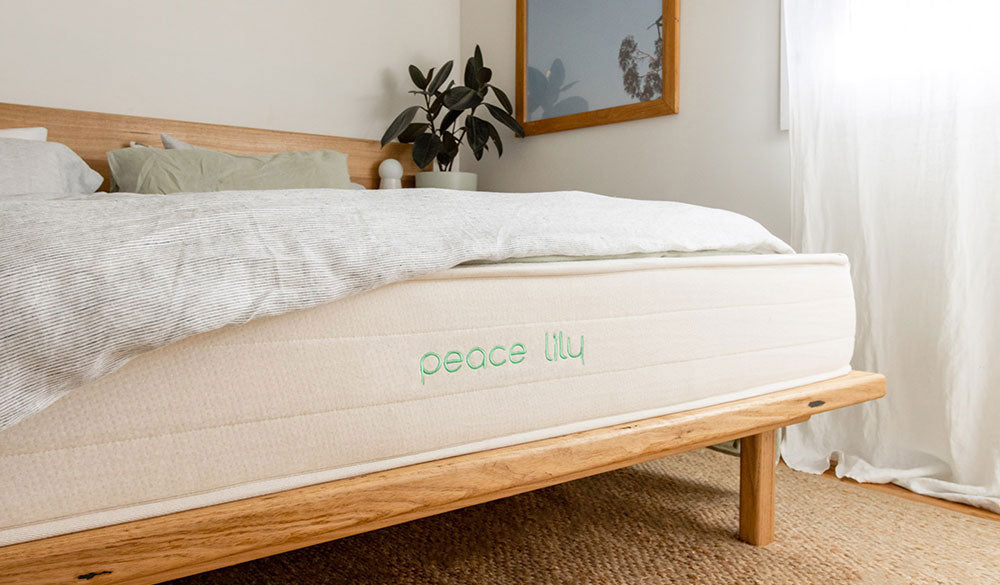 Peace Lily mattress with striped bedding on a wooden bed frame, eco-luxury you can rely on